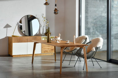 Modern gestalteter LOTTE Massivholz Esstisch aus Eiche von Whiteoak, in einem hellen, einladenden Raum, flankiert von Stühlen mit Schaffellbezügen und eleganten Wohnaccessoires