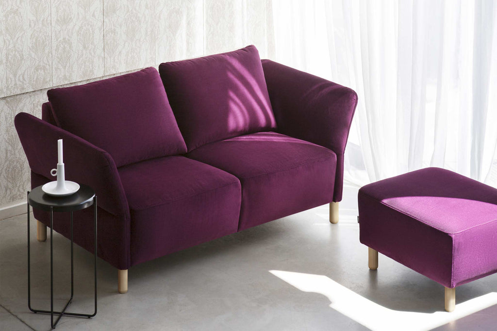 Sofa in Violett mit passendem Pouf im hellen Wohnraum