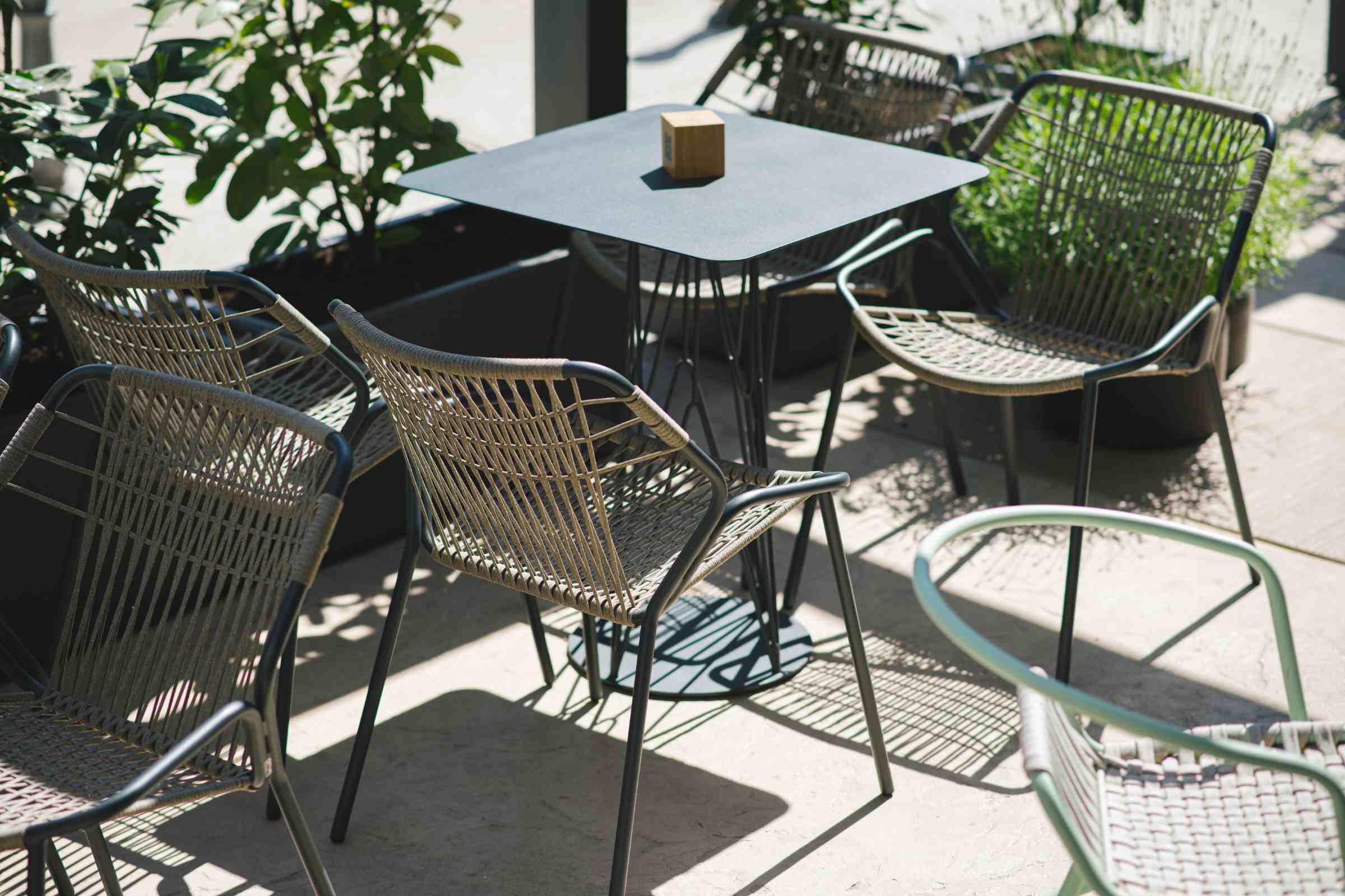 Outdoor-Szene mit mehreren stilvollen Gartenstühlen um einen quadratischen Tisch