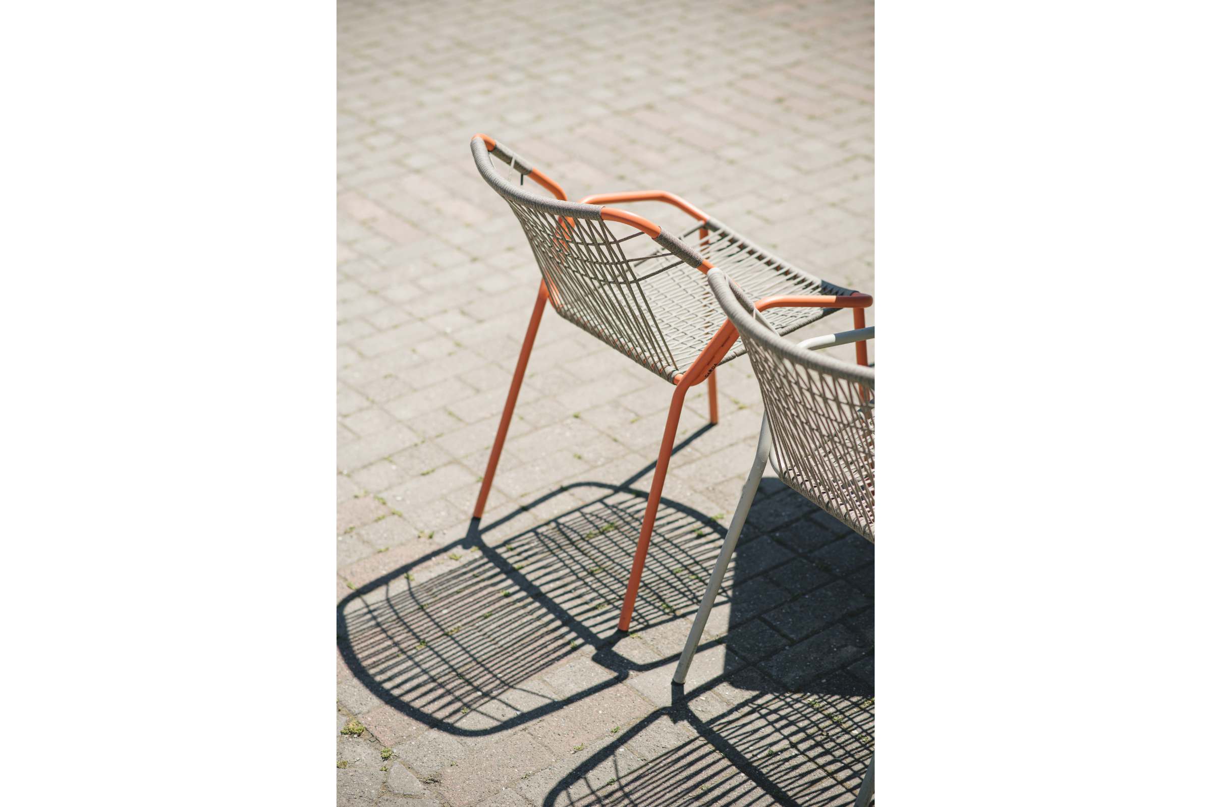 Zwei moderne Gartenstühle mit Seilbespannung im Freien auf Pflastersteinen