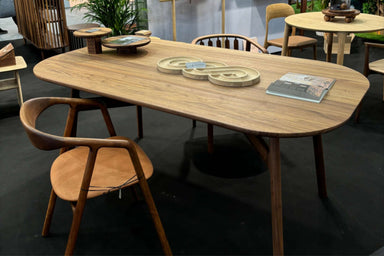 Ein MARSHALL Designer Esstisch aus Nussbaum Massivholz, oval geformt, mit einem Bled designer stuhl auf einer Ausstellungsfläche. Auf dem Tisch befinden sich dekorative Gegenstände und ein aufgeschlagenes Katalog