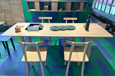 NERVOSA Designer-Esstisch von Woak in einem Raum mit mehrfarbig gemustertem Boden, umgeben von Stühlen im gleichen Design. Der Tisch ist geschmückt mit Holzutensilien, Servierschalen und einer dekorativen Flasche aus Holz