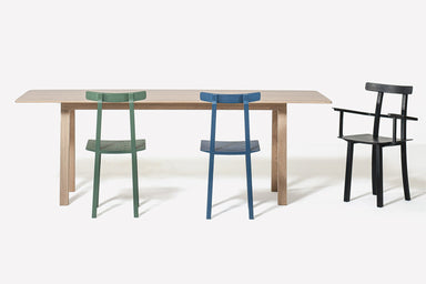 Ein Holztisch mit drei Stühlen in verschiedenen Farben vor einem weißen Hintergrund.